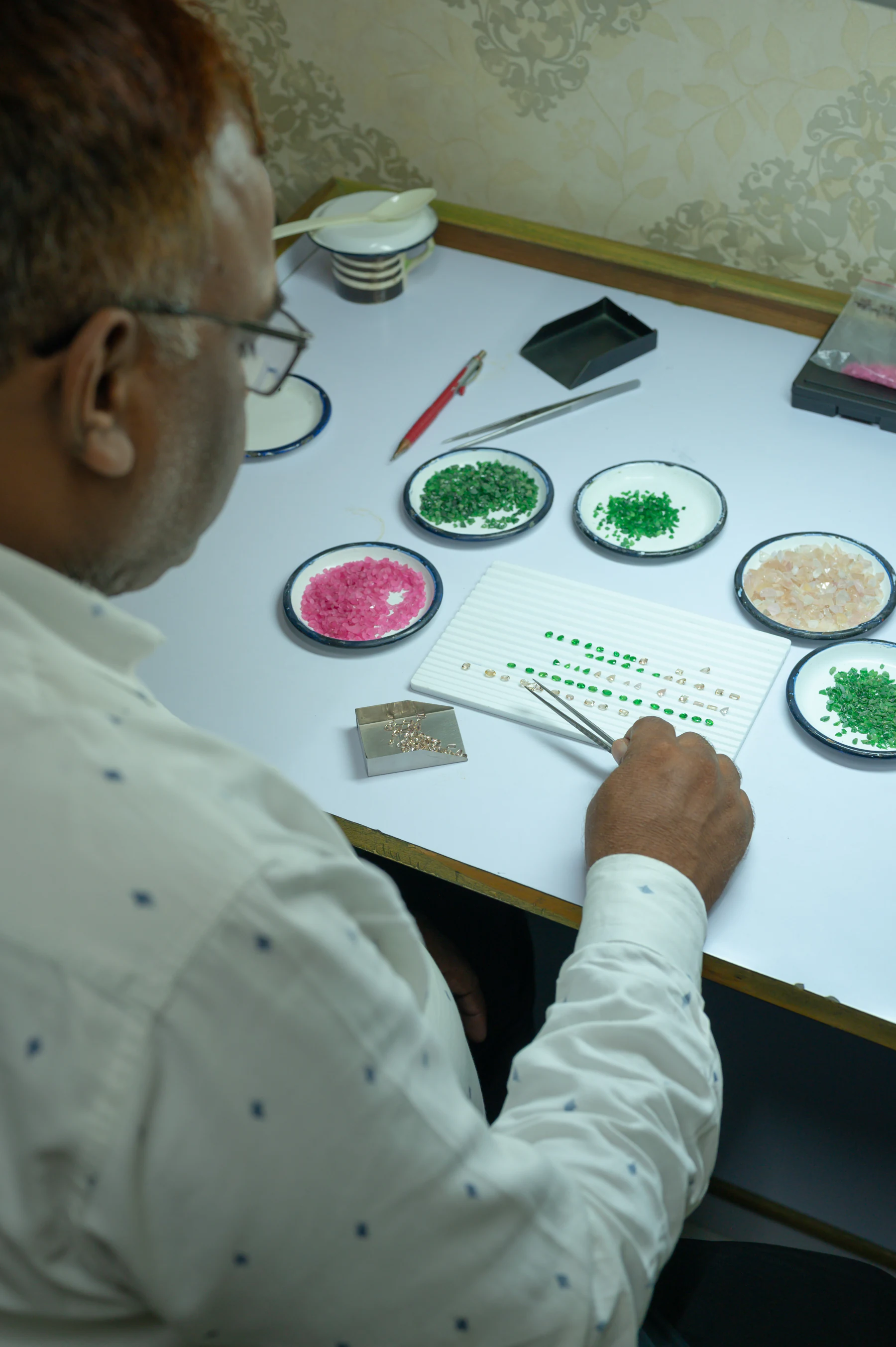 A gem sorter at a white table, grading rough tsavorite, spinel and garnet into dishes by colour.