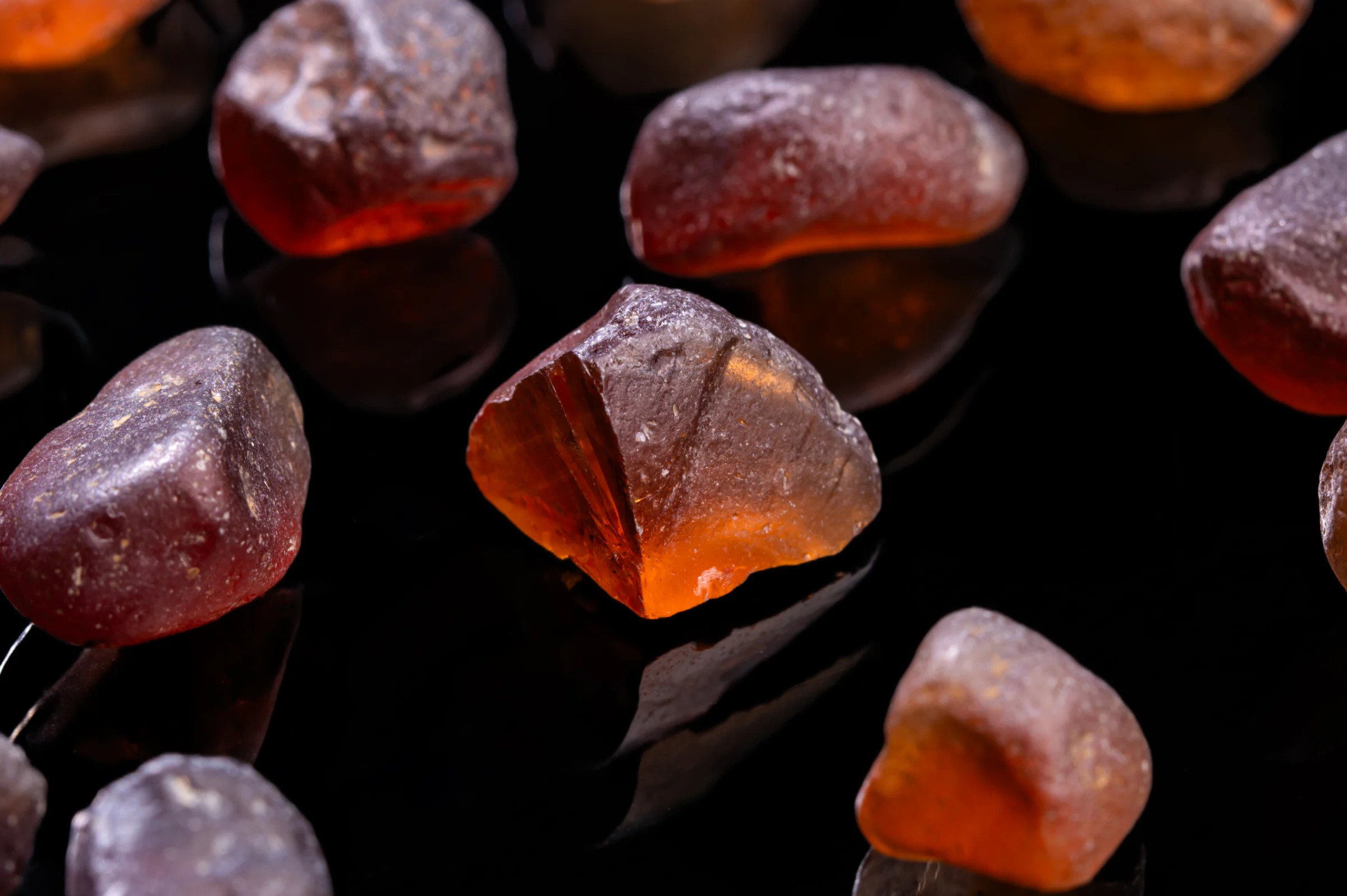 Rough Malaya garnet pebbles glowing amber on black.