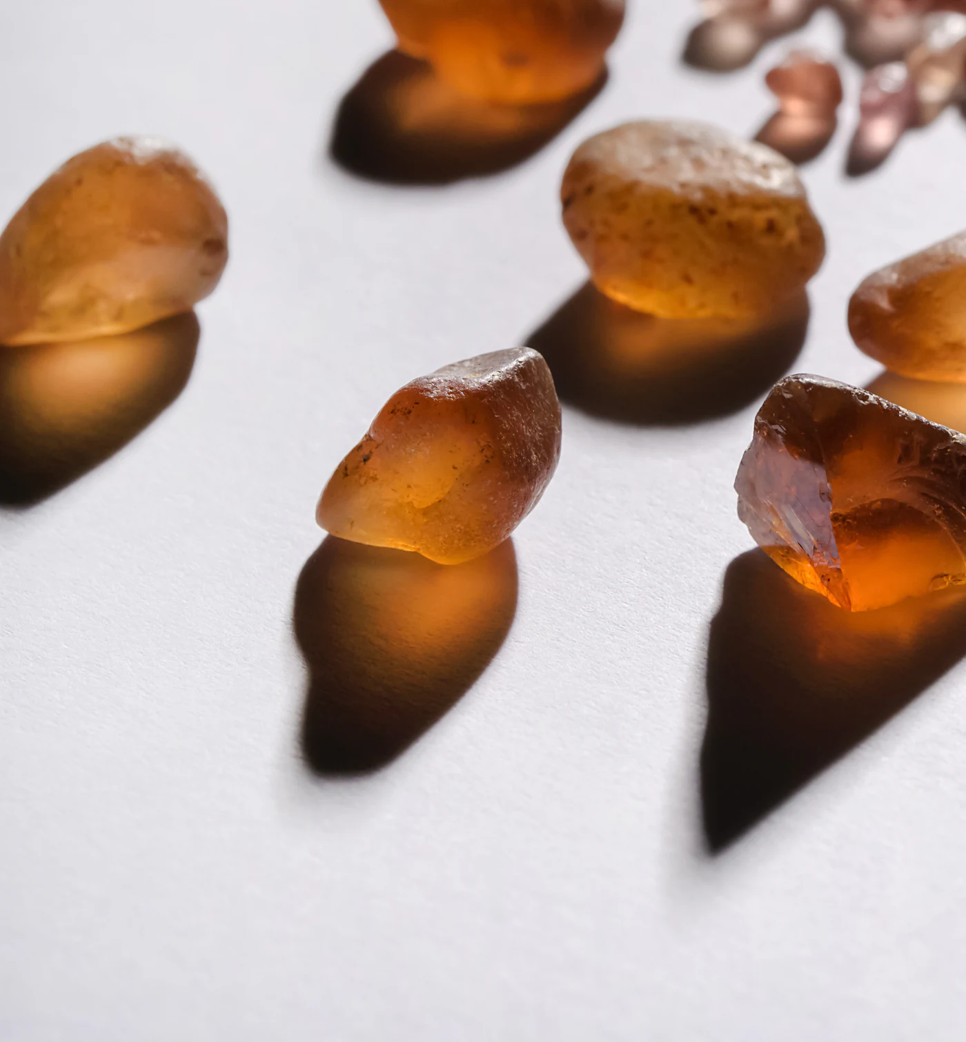 Rough Malaya garnets casting amber shadows on white.