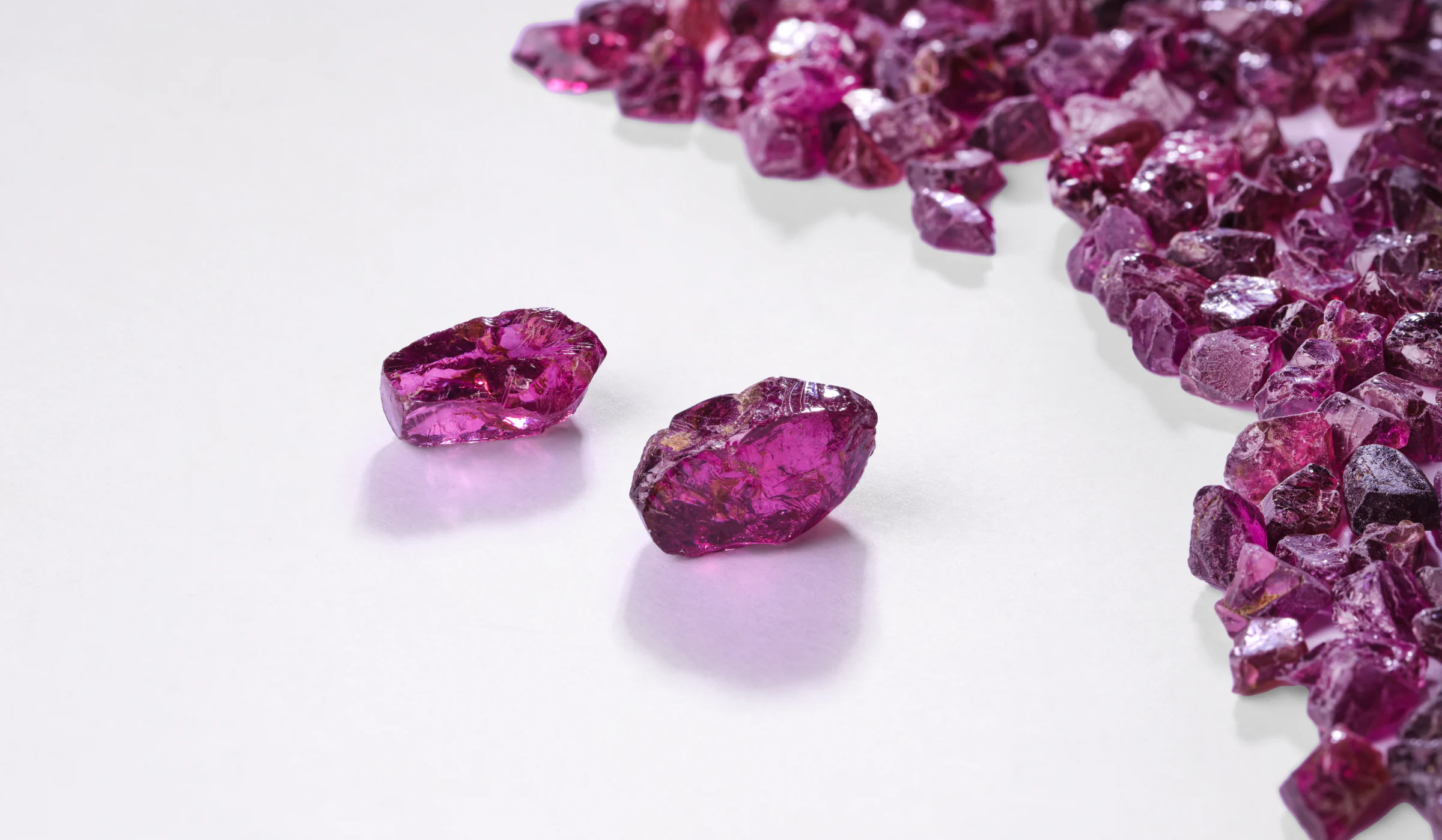 Two rough rhodolites on white, a pile of rough stones behind them.