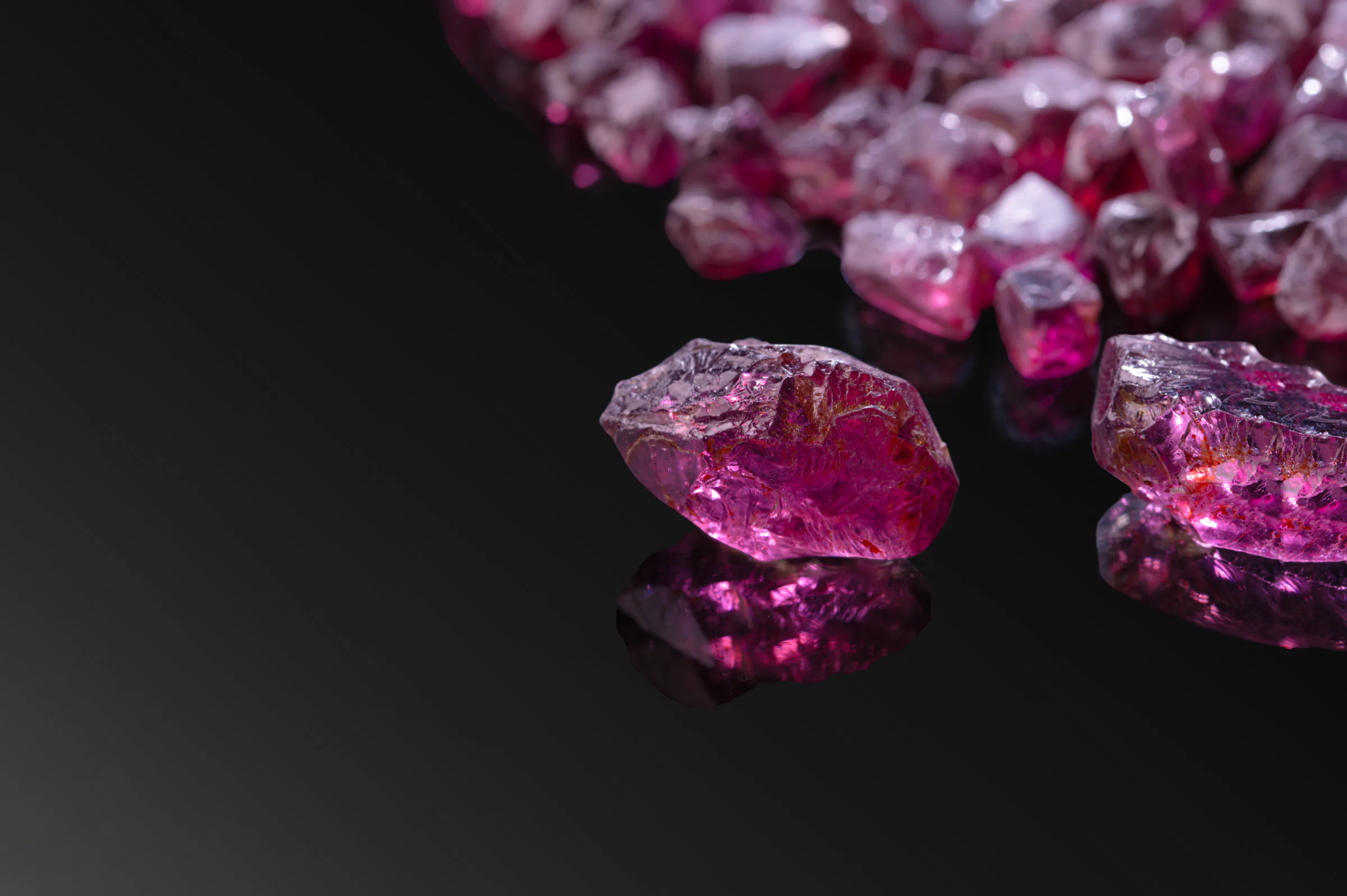 A rough rhodolite on black, reflected in the surface beneath it.