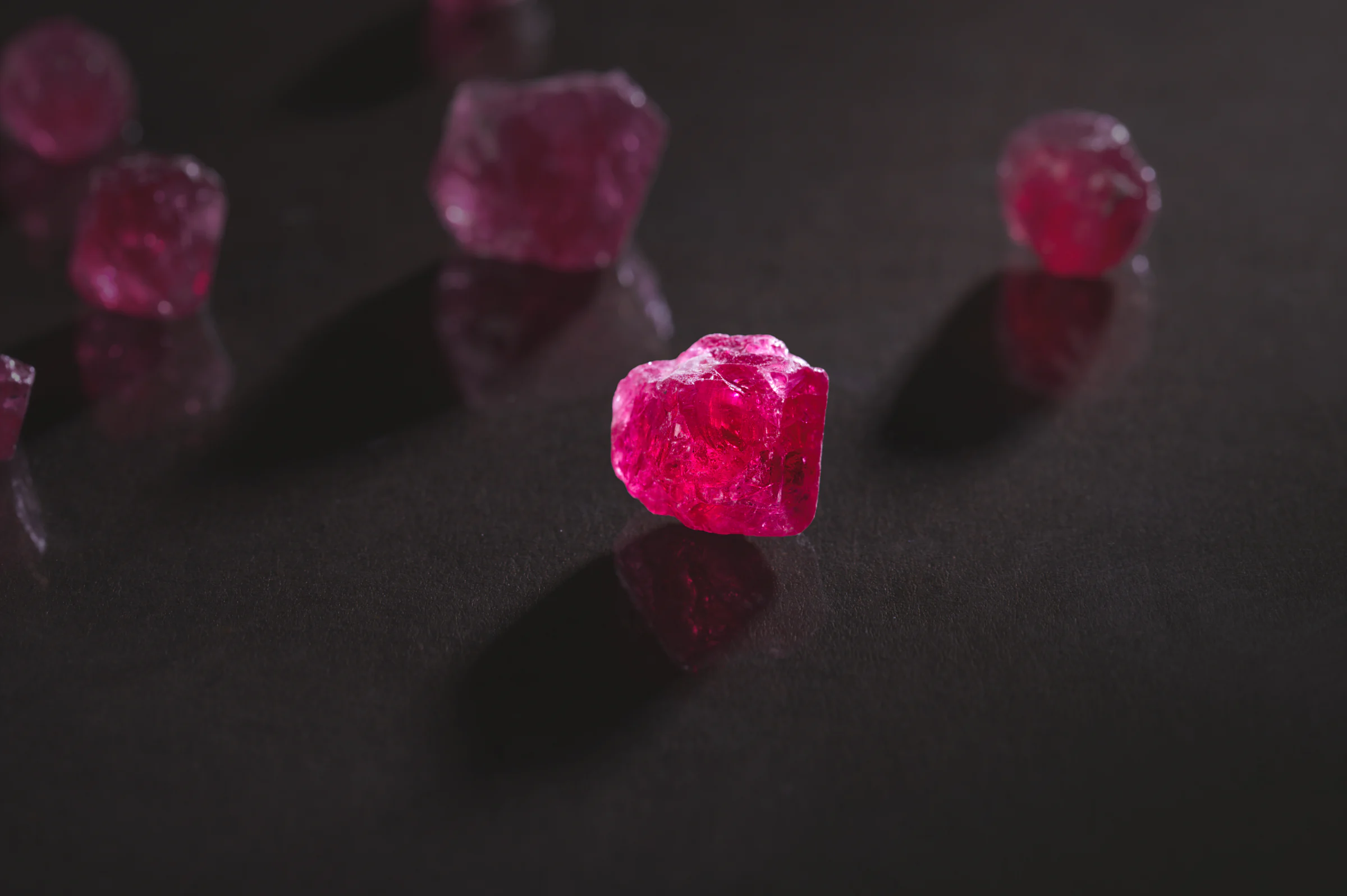 A rough pink spinel crystal on black, with more crystals out of focus behind it.