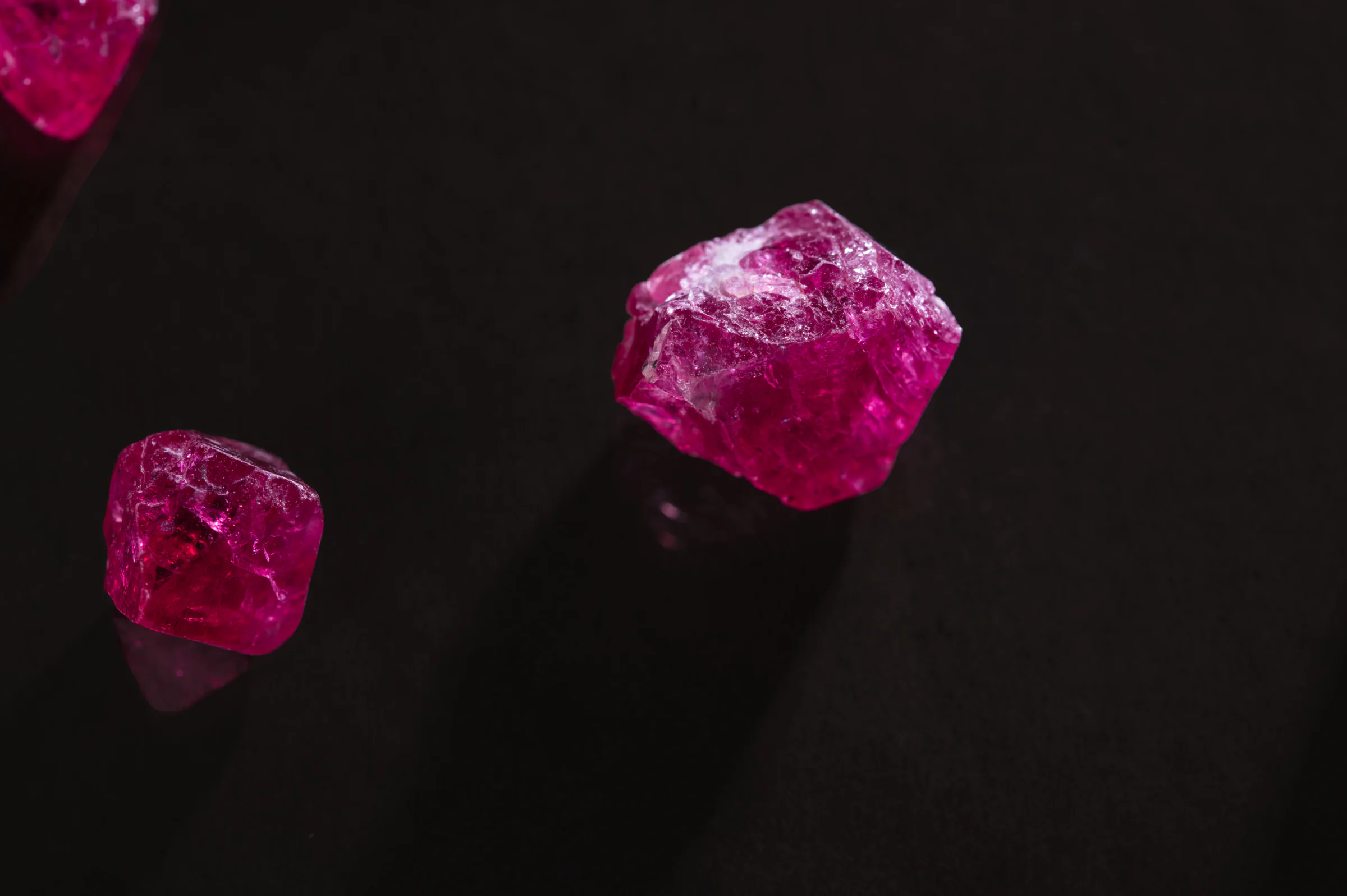 Rough pink spinel crystals on black, lit so they glow from within.