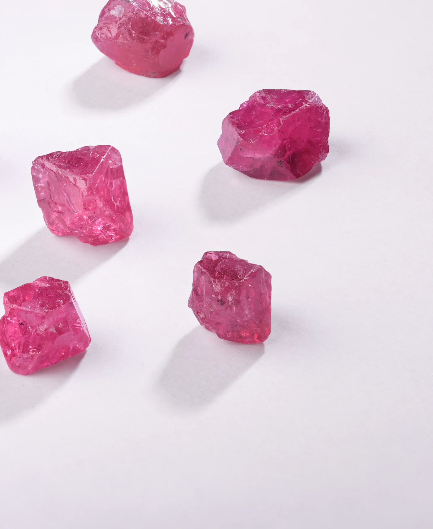 Five rough pink spinel crystals casting soft shadows on white.