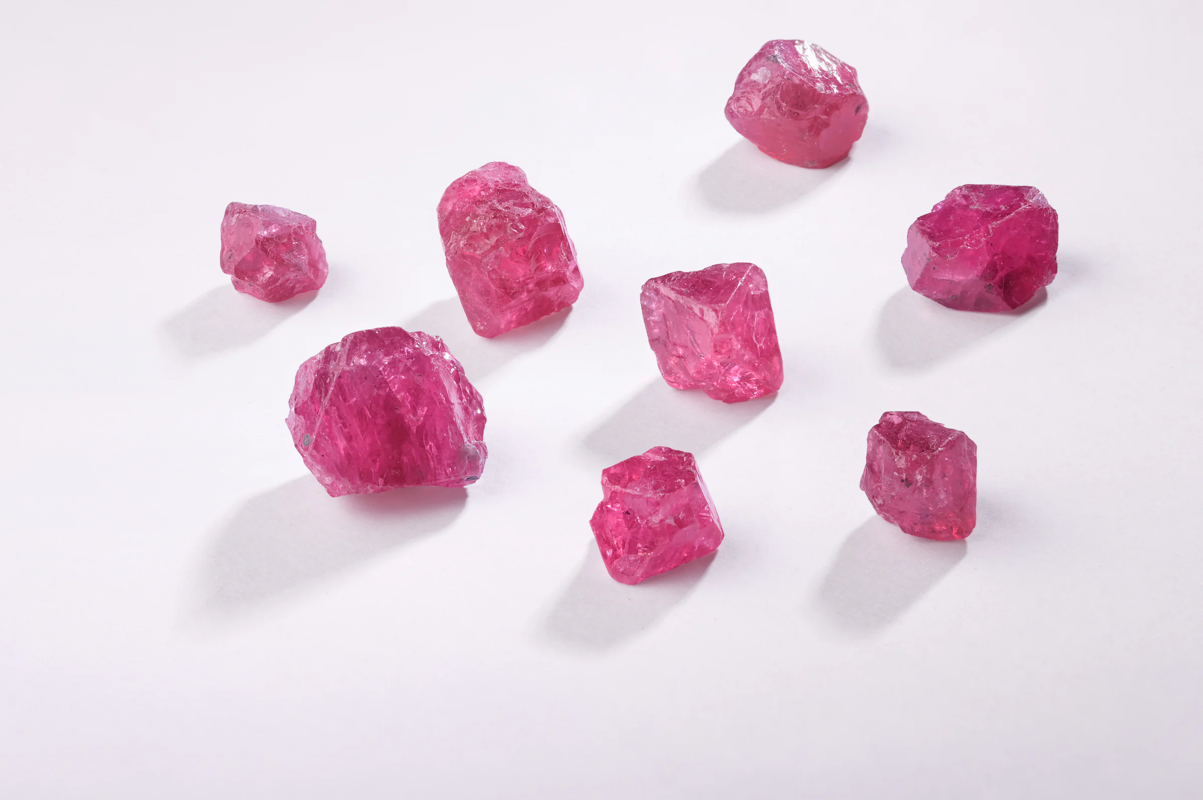Eight rough pink spinel crystals scattered on a white table.