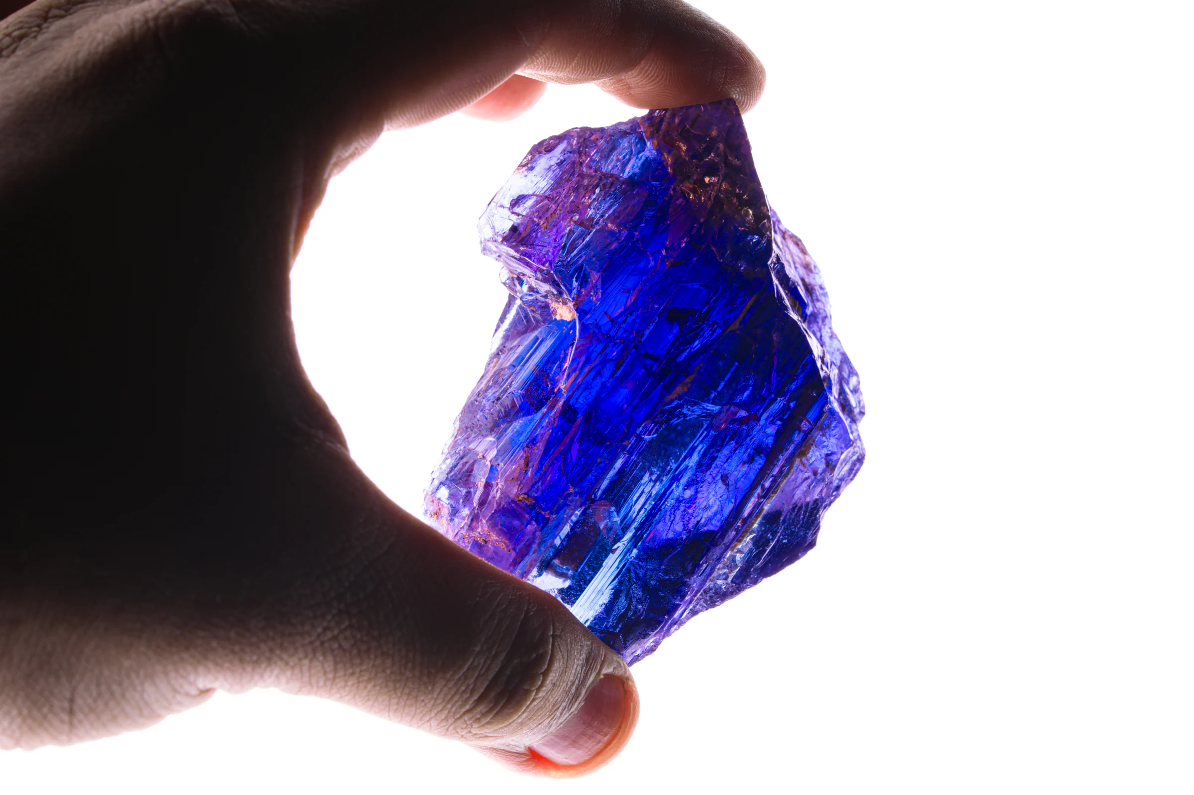 A rough tanzanite held up to the light, glowing blue and violet.