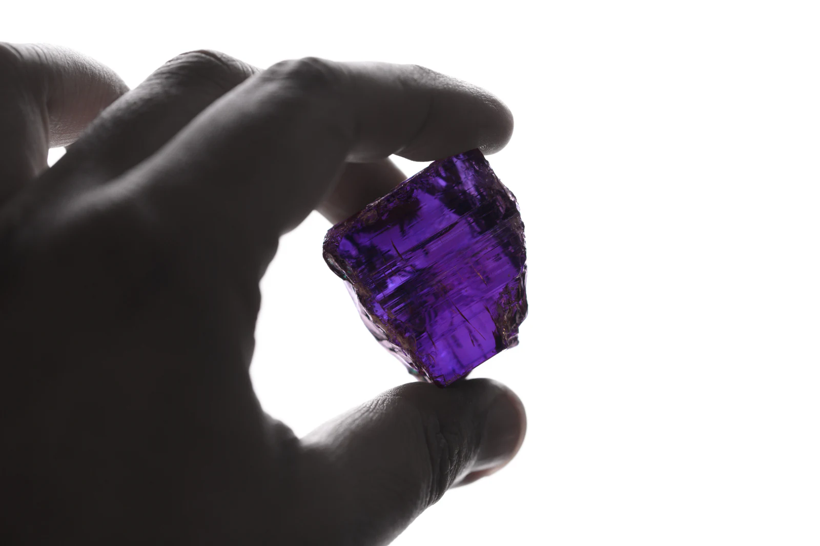 A violet rough tanzanite held between finger and thumb against the light.